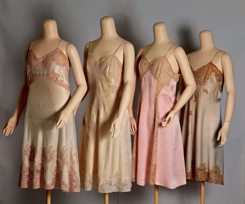 Four fitted 1930s silk full slips with shaped busts and lace insertion, displayed on museum mannequins